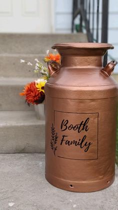 a large copper urn sitting on the side of a cement walkway next to flowers