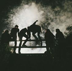 silhouettes of people standing on a fence with fireworks in the sky behind them at night