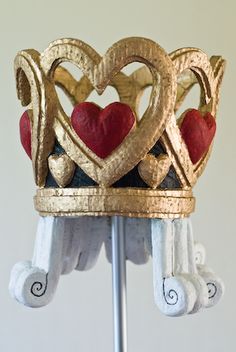 a gold crown with hearts on it is sitting on a metal stand in front of a white wall