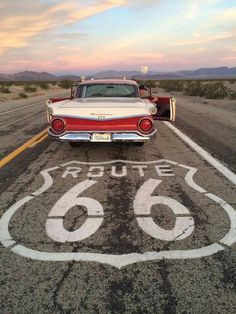 an old red and white car sitting in the middle of a road with route 66 painted on it