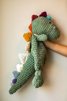 a crocheted dinosaur stuffed animal is being held by someone's hand on the wall