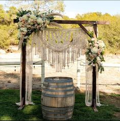 a wooden barrel with flowers and greenery on the top sits in front of a wedding arch