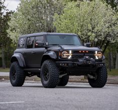 a large black truck parked on top of a parking lot with trees in the background