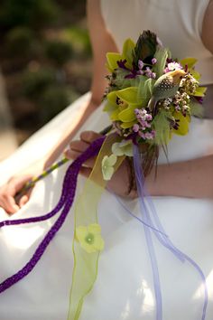 the bride is holding her wedding bouquet with purple ribbons and flowers on it's lap