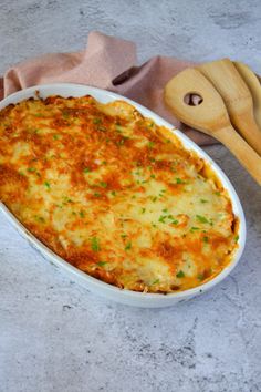 a casserole dish with cheese and parsley on the side next to two wooden utensils