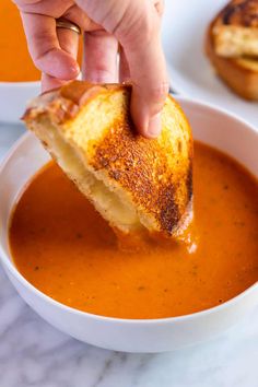 a person dipping cheese into a bowl of tomato soup with a grilled piece of bread sticking out of it