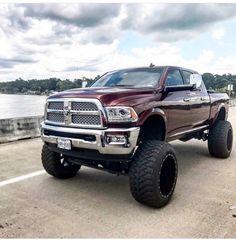 a red ram truck driving down a road next to a lake and clouds in the sky