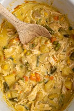 a wooden spoon in a bowl filled with chicken and veggie soup on top of a table