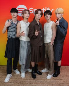 four young men standing next to each other in front of a red and orange wall