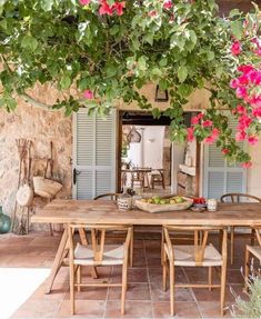 a wooden table sitting under a tree filled with pink flowers next to a stone building