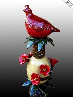 a red bird is sitting on top of a vase with flowers in it's bottom