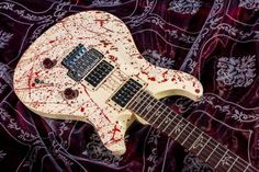 an electric guitar covered in blood on top of a purple cloth with red paint splattered all over it