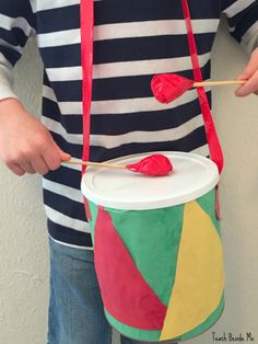 a person is holding a drum with sticks and yarn on it, while wearing a striped shirt