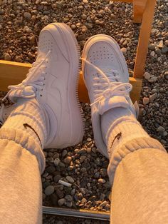 a person wearing white sneakers standing on gravel with their legs crossed and one foot in the air