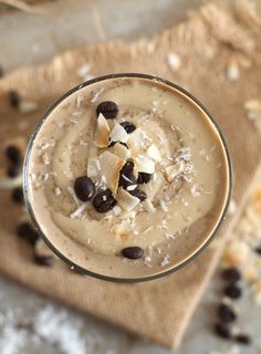 a close up of a dessert in a glass on a table with chocolate chips and coconut