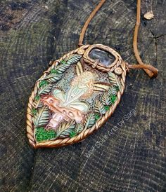 "This beautiful marquis-shaped statement piece merges Elven and Celtic aesthetics, and features a beautiful Rainbow banded Fluorite cabochon above the imprint of a ethereal copper-haired Faery seated on a toadstool! There's also hand-sculpted leaf accents, and hand twisted border accents. The colors are in green, copper, and bronze! It is shown with the tan satin cord! To invite this piece into your life is to invite in a little bit of magick! Each piece is a one-of-a-kind that is created with i Handmade Polymer Clay Jewelry In Fantasy Style, Fantasy Polymer Clay Jewelry As A Gift, Artistic Polymer Clay Pendant Jewelry, Handmade Nature-inspired Polymer Clay Jewelry, Handmade Polymer Clay Jewelry For Collectors, Artistic Polymer Clay Jewelry For Crafting, Collectible Handmade Resin Jewelry, Spiritual Polymer Clay Jewelry For Crafting, Artisan Resin Pendant Jewelry