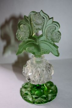 a glass vase with flowers in it on top of a green base and leaves sticking out of the bottom