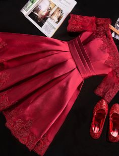 a red dress and shoes on a black surface next to a cell phone, magazine, and other items