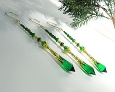 three pairs of green and gold earrings on a white surface next to a pine tree