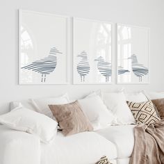 a white couch with pillows and blankets on top of it next to two framed pictures