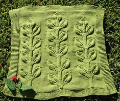 a green knitted blanket sitting on top of grass next to a red flower and leaf