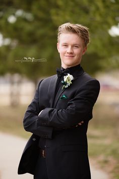 a young man in a tuxedo is posing for a photo with his arms crossed