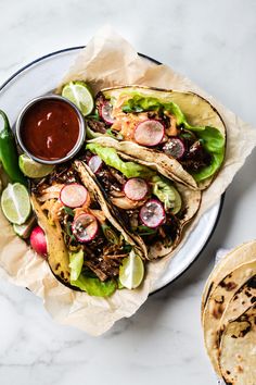 three tacos with meat, lettuce and radishes on a plate