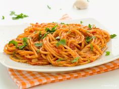 a white plate topped with spaghetti on top of a checkered cloth next to garlic and parsley