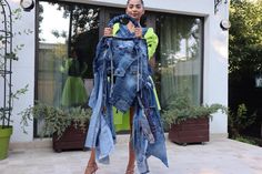 a woman is holding up an old pair of jean jackets in front of her house