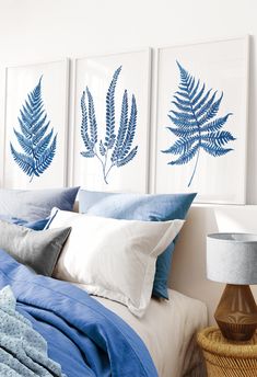 three blue and white prints on the wall above a bed in a bedroom with pillows