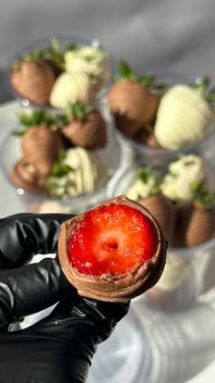 a hand holding a chocolate covered strawberry in front of other desserts