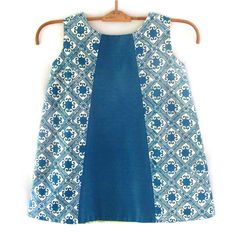 A classic little A-line dress-shape in a fresh mix of bright turquoise, hand-stamped Indonesian batik and two-tone cotton blend. Fully-lined with a back button enclosure. Size: 24-36 months 100% cotton Cold water wash; hang dry out of direct sunlight Blue Batik Print Dress For Spring, Fitted Blue Dress With Block Print, Blue A-line Dress With Patchwork, Green Cotton Dress With Batik Print, Blue Cotton Dress With Batik Print, Fitted Blue Block Print Dress, Green Cotton Batik Print Dress, Blue Sleeveless Dress With Batik Print, Blue Cotton Batik Print Dress