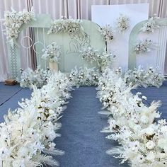 an arrangement of white flowers and greenery on a blue carpeted floor in front of a backdrop