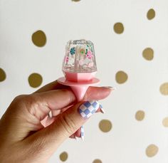 a hand holding a pink and white object with polka dots on the wall behind it