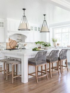 a large kitchen with white cabinets and wooden stools in front of an island counter