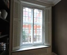 an empty room with open shutters and bookshelves on the wall, in front of a window