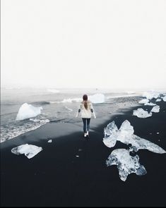 a woman walking on the beach with ice flakes floating in the water behind her