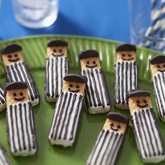 there are many small cookies made to look like men in hats and striped clothes on a green plate