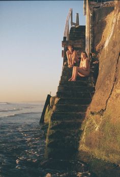 two women are sitting on the steps by the ocean