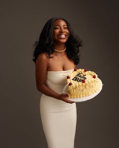 a woman in a white dress holding a cake with writing on it and smiling at the camera