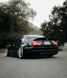 a black car parked on the side of a road with trees in the back ground