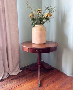 a vase with flowers on top of a wooden table in front of a curtained window