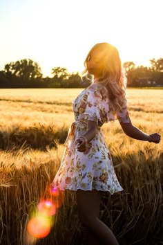 a woman in a dress is walking through a wheat field with the sun behind her