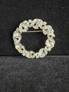 This circle brooch has entwining rows of small rhinestones around large rhinestones that catch all the lights to reflect beauty. There is a signature on the back but I couldn't make it out. Please look at the pictures carefully as this is the item you're purchasing.  I do combine shipping on multiple items. Elegant Round Brooches With Rhinestones, Elegant Round Rhinestone Brooches, Crystal Round Brooch For Party, Round Crystal Brooch For Party, Anniversary Rhinestone Round Brooches, Anniversary Brooches With Rhinestones, Anniversary Round Brooches With Rhinestones, Anniversary Round Rhinestones Brooches, Silver Rhinestone Round Brooches