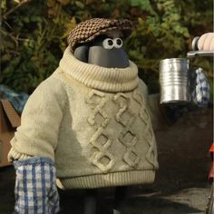 a stuffed animal wearing a sweater and hat next to a coffee cup on a table