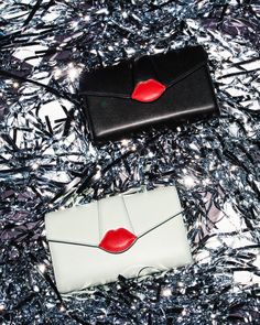 two black and white purses sitting on top of a silver foiled surface with red lips painted on them