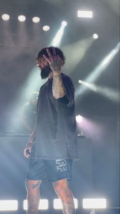 a man standing on top of a stage holding his hand up to the side with lights behind him