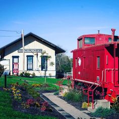 a red train car sitting in front of a white house