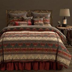 a bed with a red and brown comforter on top of it next to a night stand