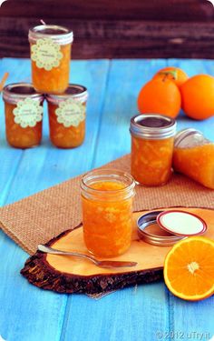 three jars filled with orange jam sitting on top of a wooden table next to sliced oranges